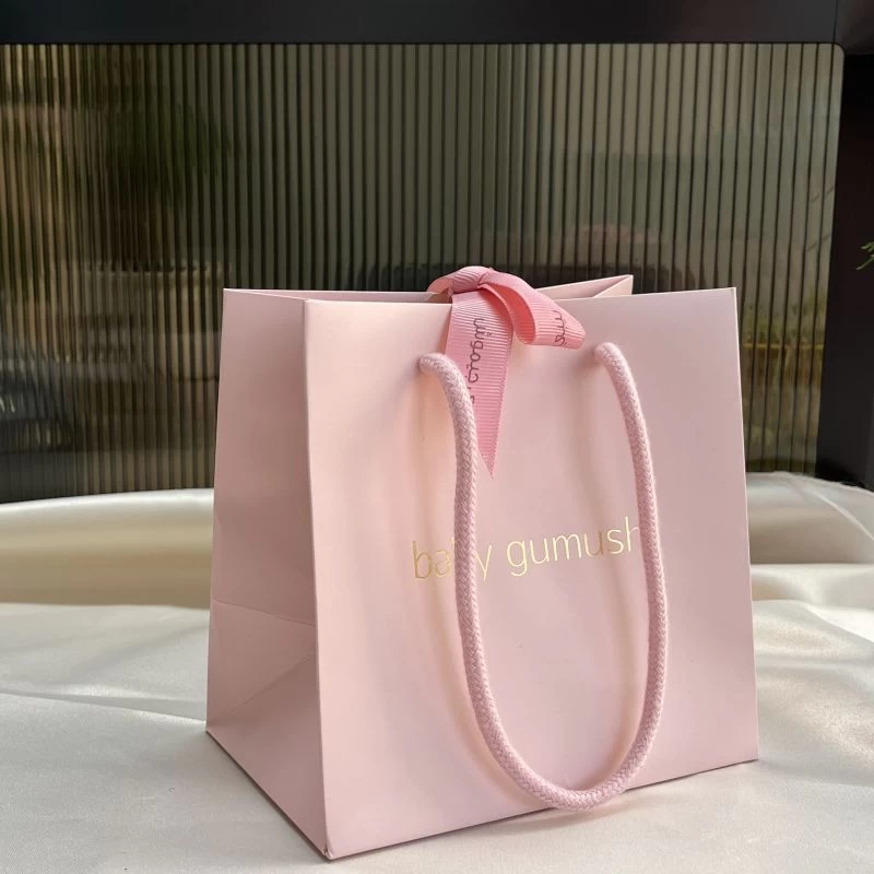 Bolsa de regalo rosa para embalaje de joyas con cinta en el centro.