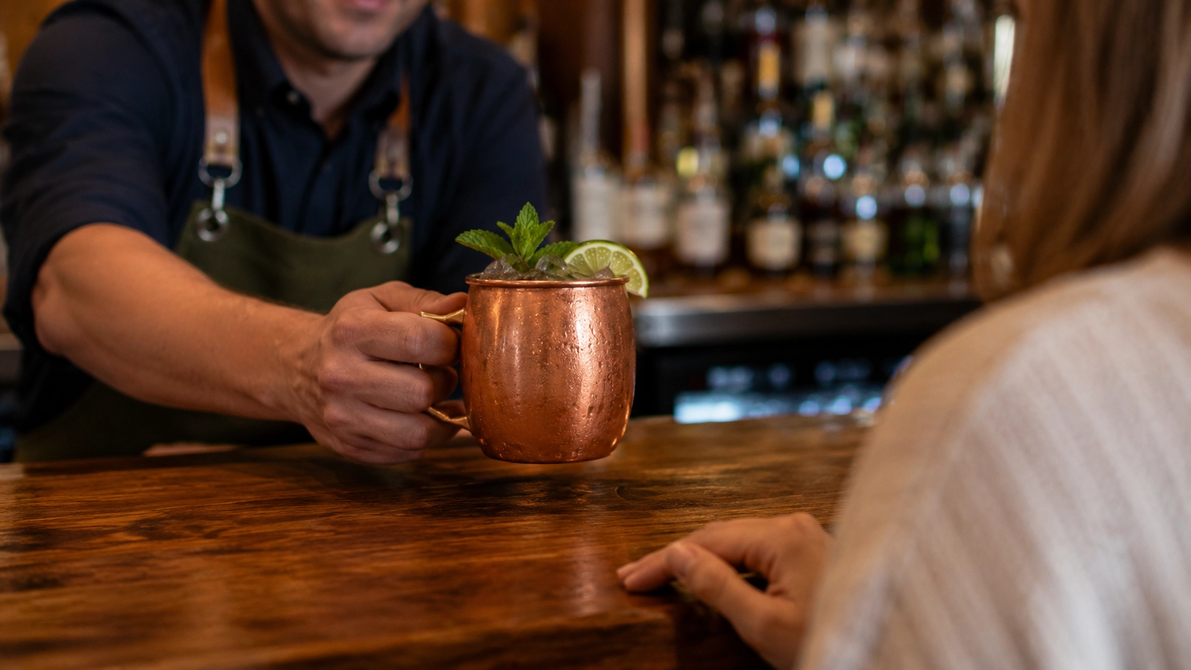Bartender serving a chilled Moscow Mule in a copper mug with ice, lime, and mint.