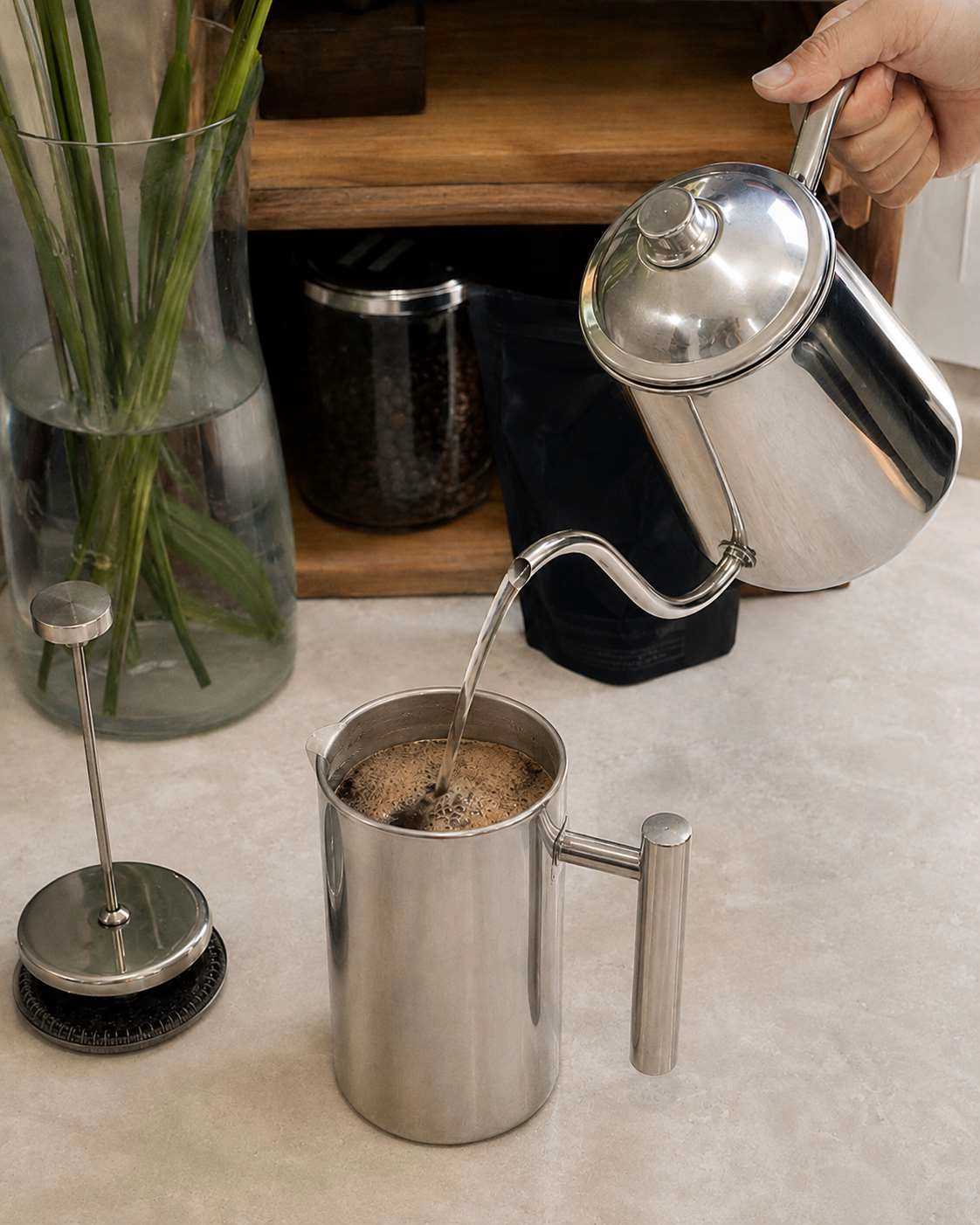 Hot water being poured into a stainless steel French press during the brewing process.