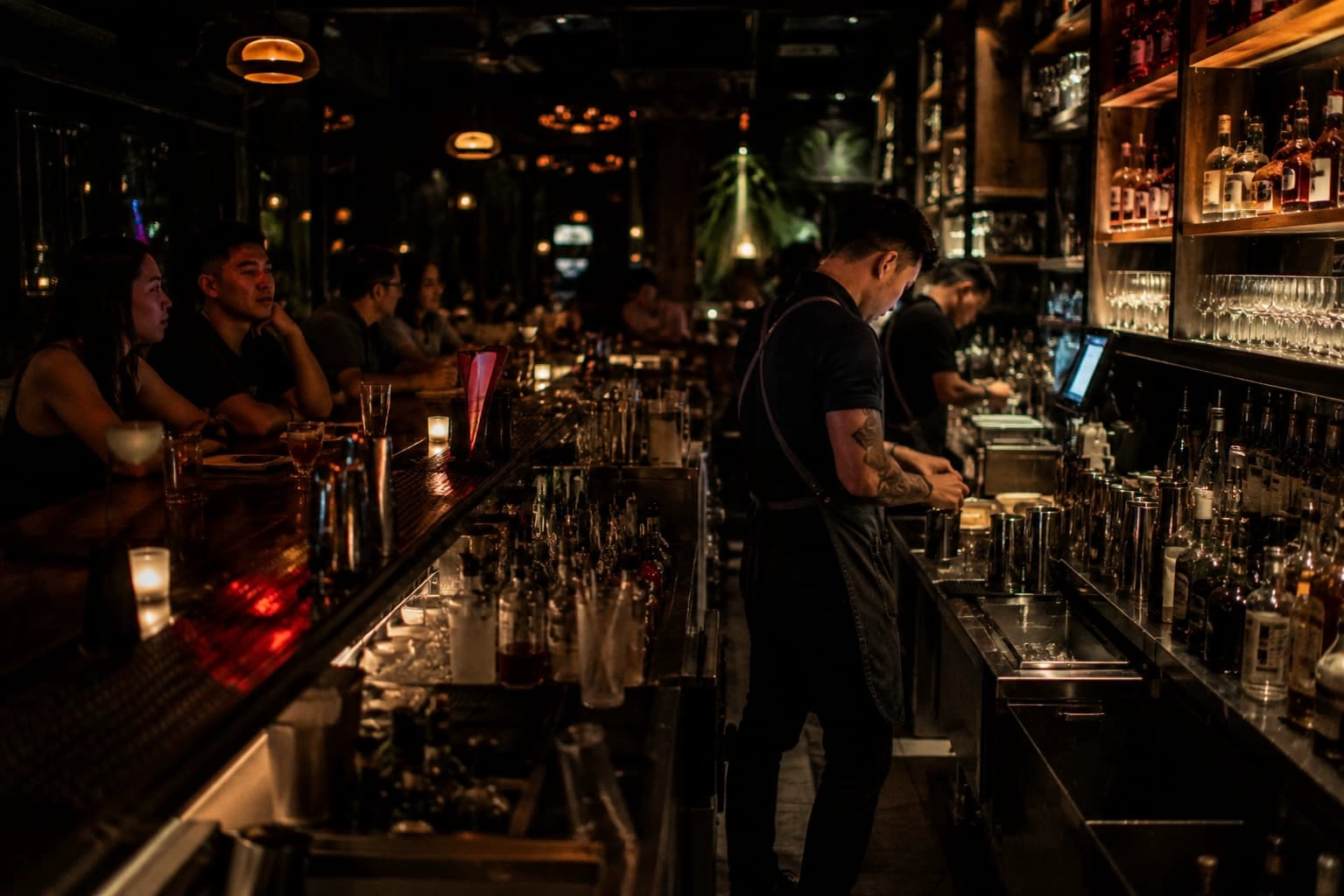 Busy commercial cocktail bar during evening service with bartenders working behind the counter and guests seated along the bar
